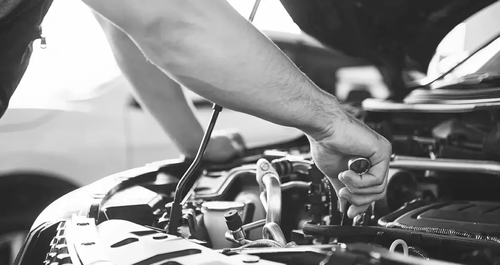 Mechaniker arbeitet mit einem Ringschlüssel im Motorraum eines Fahrzeugs bei geöffneter Haube; Nahaufnahme in Schwarz-Weiß.