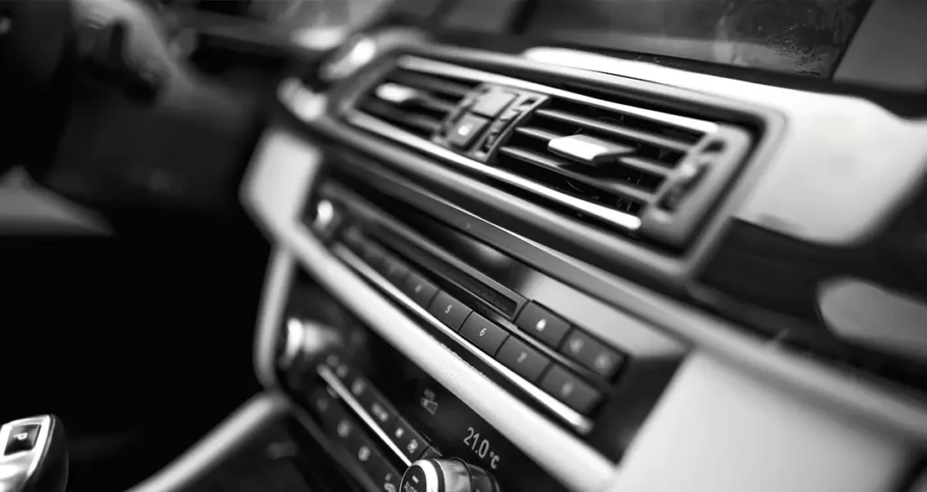 Innenraumdetail eines Fahrzeugs: Lüftungsdüse und Mittelkonsole mit Tastenreihe und Klimabedienung, Display zeigt 21,0 °C.